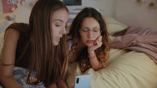 两个女人趴在床上看手机视频素材模板下载