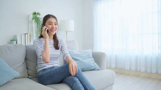 亚洲美女坐在沙发上，在家里打手机。