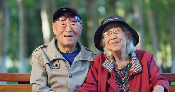 幸福的老年夫妇坐在公园长椅上面带笑容聊天