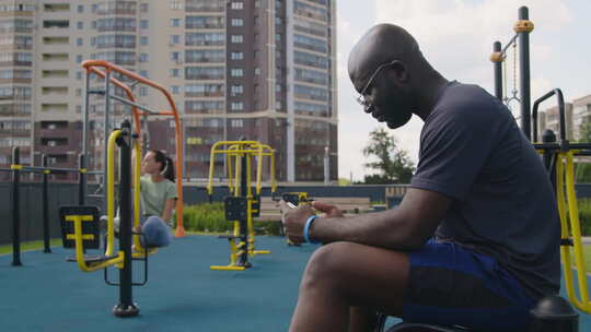 戴眼镜的运动员在运动场看电话锻炼视频