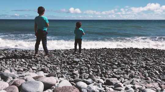 马德拉岛火山海滩上，孩子们向海里扔石头。静态镜头。视频素材模板下载