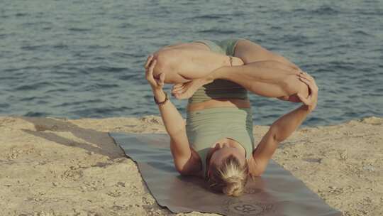 金发白人女性瑜伽老师练习和掌握倒莲花姿势在前面的悬崖上