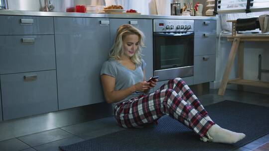 女孩坐在厨房地板上玩手机
