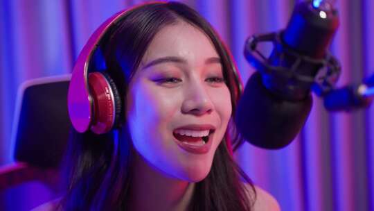 亚洲年轻的音频DJ女人在麦克风上唱一首歌来广播。