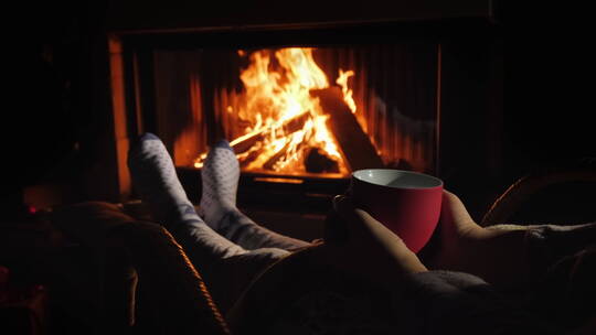 女人躺在躺椅上抱着茶杯在壁炉前取暖