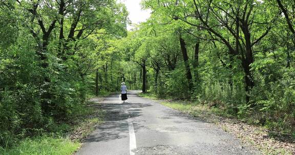 女人沿着公园森林小路悠闲散步背影