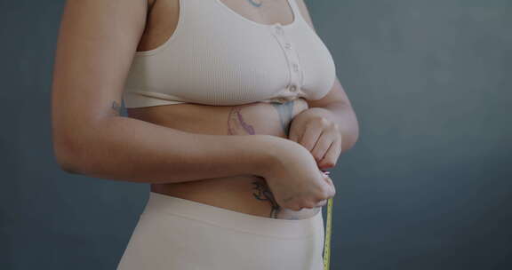 灰色背景下用卷尺测量腰围的女性手特写