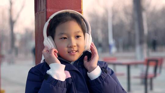 实拍冬季坐在公园长廊带耳机欣赏音乐的女孩