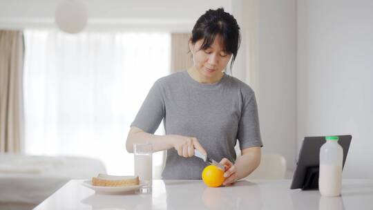 早晨年轻女孩厨房台子上切橙子做早餐看视频