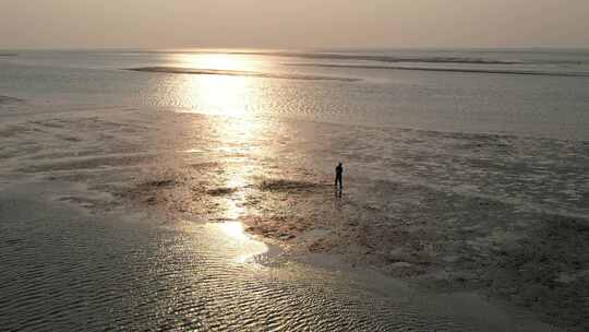 一个人行走在夕阳照耀下的沙滩上