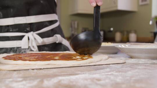 男性在披萨面团上涂抹番茄酱特写