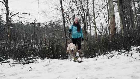 一个女人带着她的狗在白雪覆盖的森林里散步