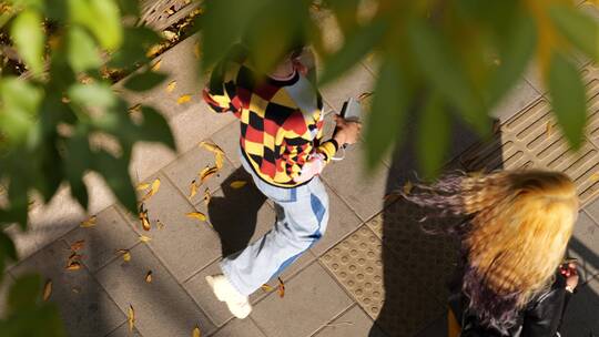 俯拍秋天里人行道上行人走在落满黄叶的路上