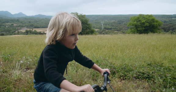 可爱的快乐儿童男孩在乡村公路上骑自行车