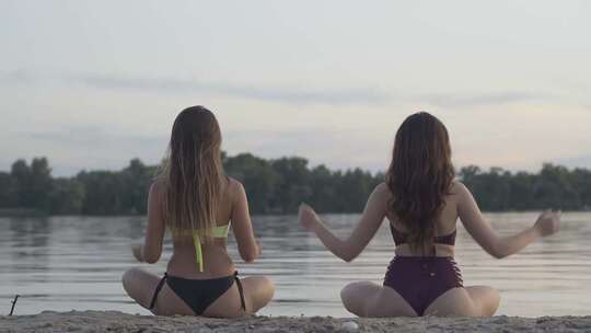 两个穿比基尼的女孩在湖边冥想瑜伽