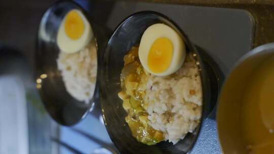 奶油豆腐咖喱舀进黑色碗里，里面有鸡蛋和米