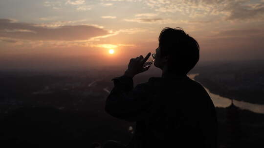 男孩在山顶看风景喝水看日落日出看夕阳背影