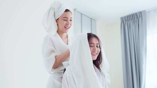 亚洲美丽的女同性恋夫妇在卧室里的床上淋浴后干燥女朋友的头发。