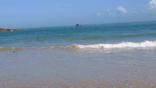 海面波浪翻涌远处有渔船的海滩景色