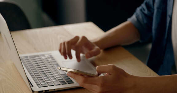 男人的腹部在智能手机上发短信，在办公桌上使用笔记本电脑