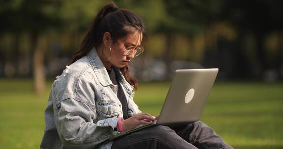 一位女大学生坐在校园草地上用笔记本电脑