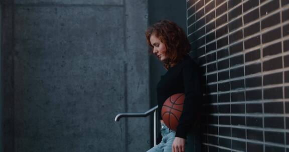 女人手持篮球倚在墙边