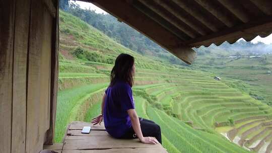 女人坐在山上，背景是田野