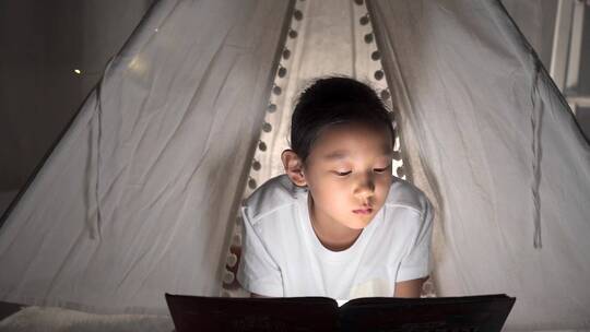 夜晚趴在帐篷里读书的亚洲女孩