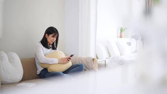 周末早晨年轻女孩坐在客厅沙发上玩智能手机视频素材模板下载
