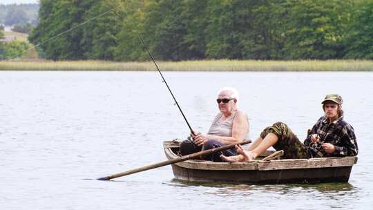 老垂钓者带着孙子坐在湖上的船上钓鱼