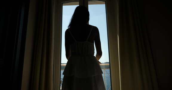 一个年轻晒黑的赤脚女人穿着白色连衣裙朝窗