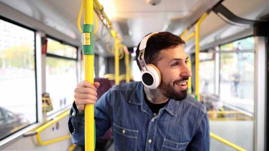 阳光明媚的公共汽车旅行中戴着耳机的微笑男