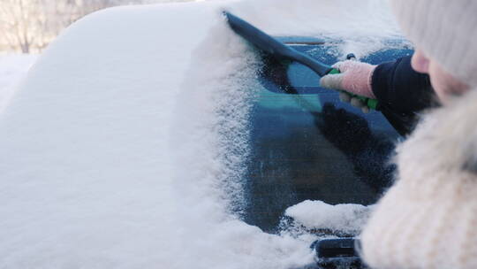 女人用刷子扫除车窗上的积雪
