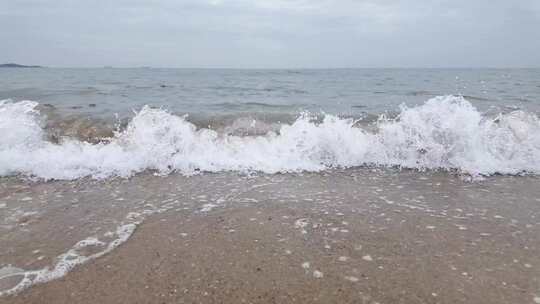 阴天海边清澈的海水拍打在沙滩上