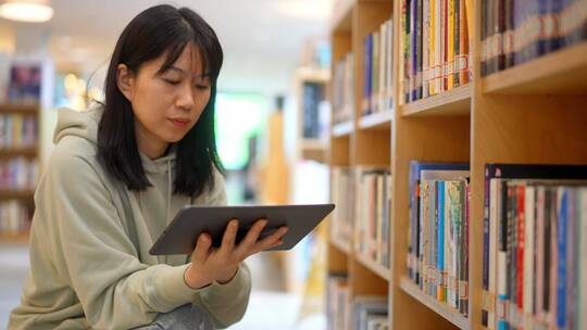 年轻女子在图书馆使用平板电脑找书