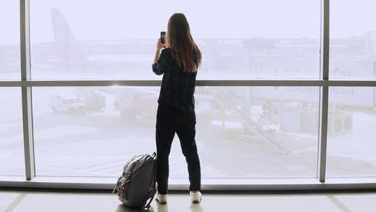 女子站在机场窗口 用手机拍照