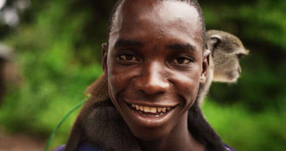 一个真实的非洲男人看着相机，抱着一只小猴