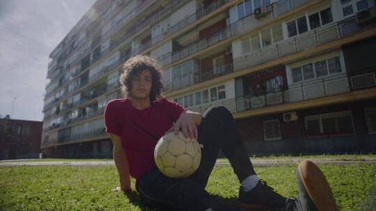 男孩抱着足球坐在草坪上休息