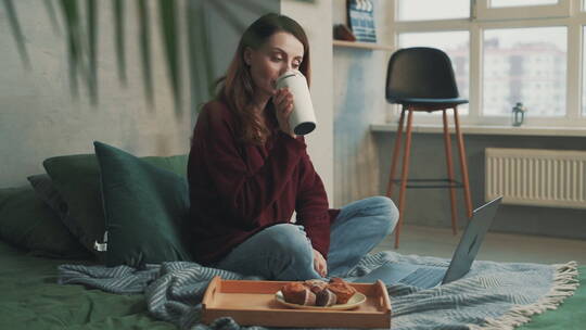 女人坐在地毯上喝着咖啡看电脑