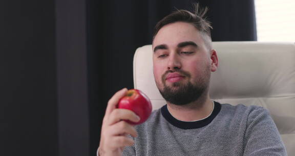 饥饿的男人坐在桌子前吃红苹果