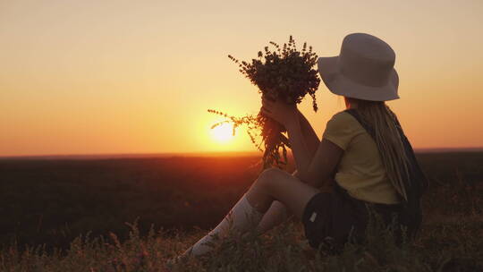 戴帽子的女孩坐在草地上欣赏日落