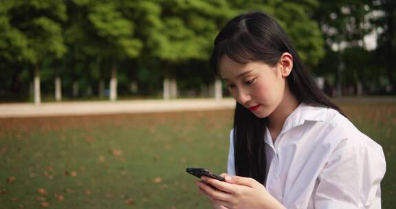 清爽美丽女大学生坐在草地上看手机
