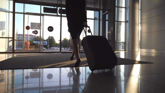 穿着高跟鞋的年轻女子提着手提箱在机场大厅或候机室散步