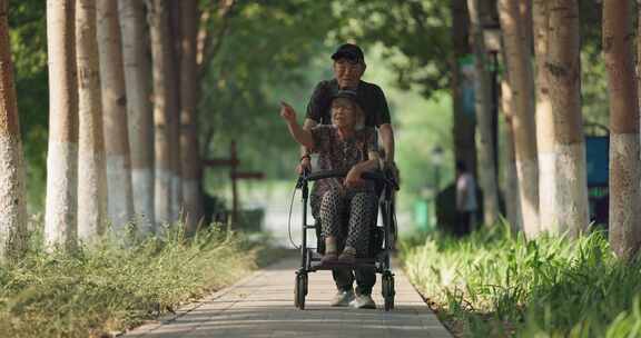 老年丈夫推着坐在轮椅上的妻子在公园散步