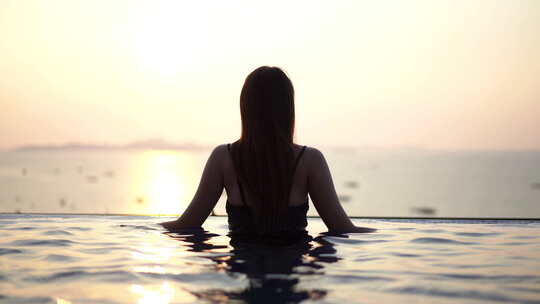 日落时，无边泳池中俯瞰海中船只的女人剪影
