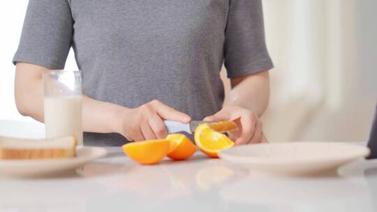 早晨年轻女孩厨房台子上切橙子做早餐看视频