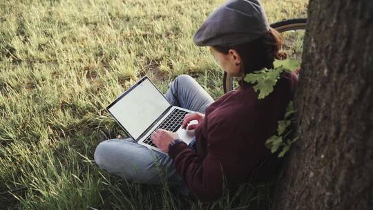 女人坐在草地上使用笔记本电脑