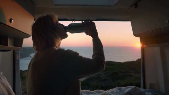 日落时，坐在敞篷露营车里喝烧瓶里的女人