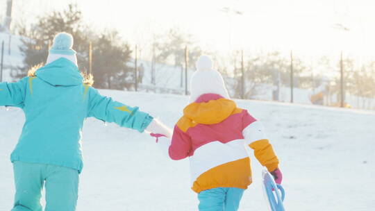 妈妈和女儿拿着雪盘在雪地里奔跑
