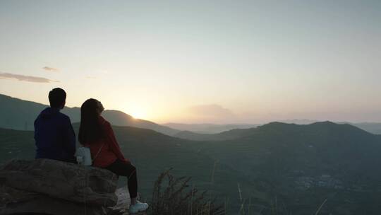情侣在山顶大石头上看夕阳